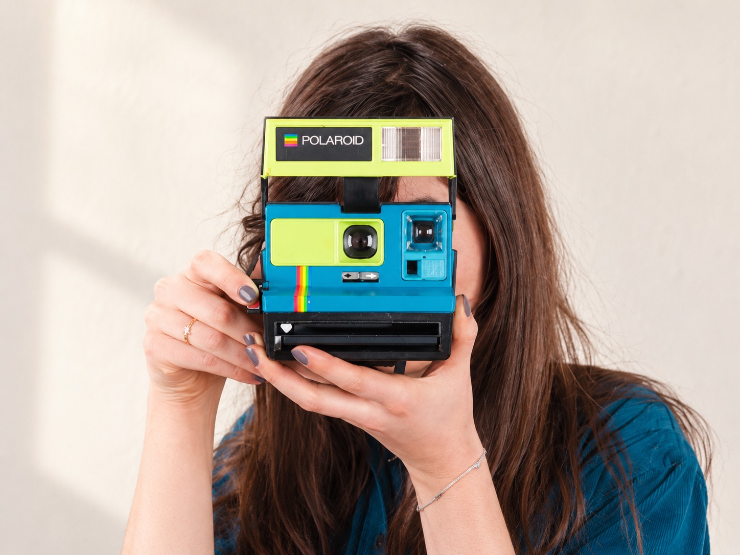Un Polaroid bleu et vert tenu devant le visage